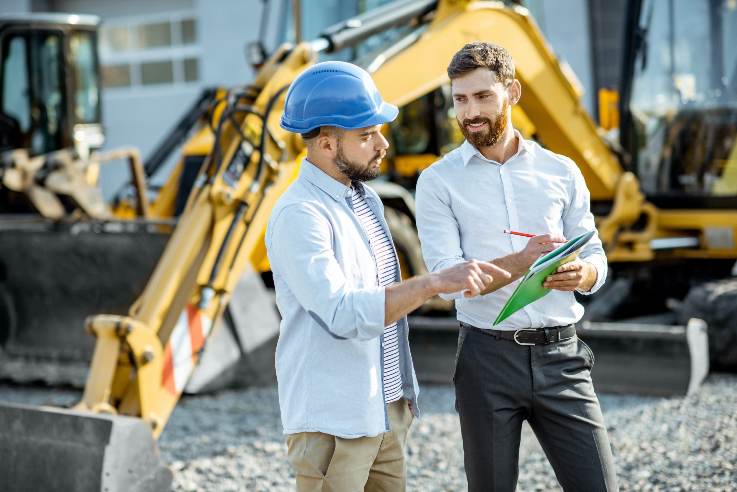 Builder choosing heavy machinery for construction with a sales consultant standing with some documents on the open ground of a shop with special vehicles