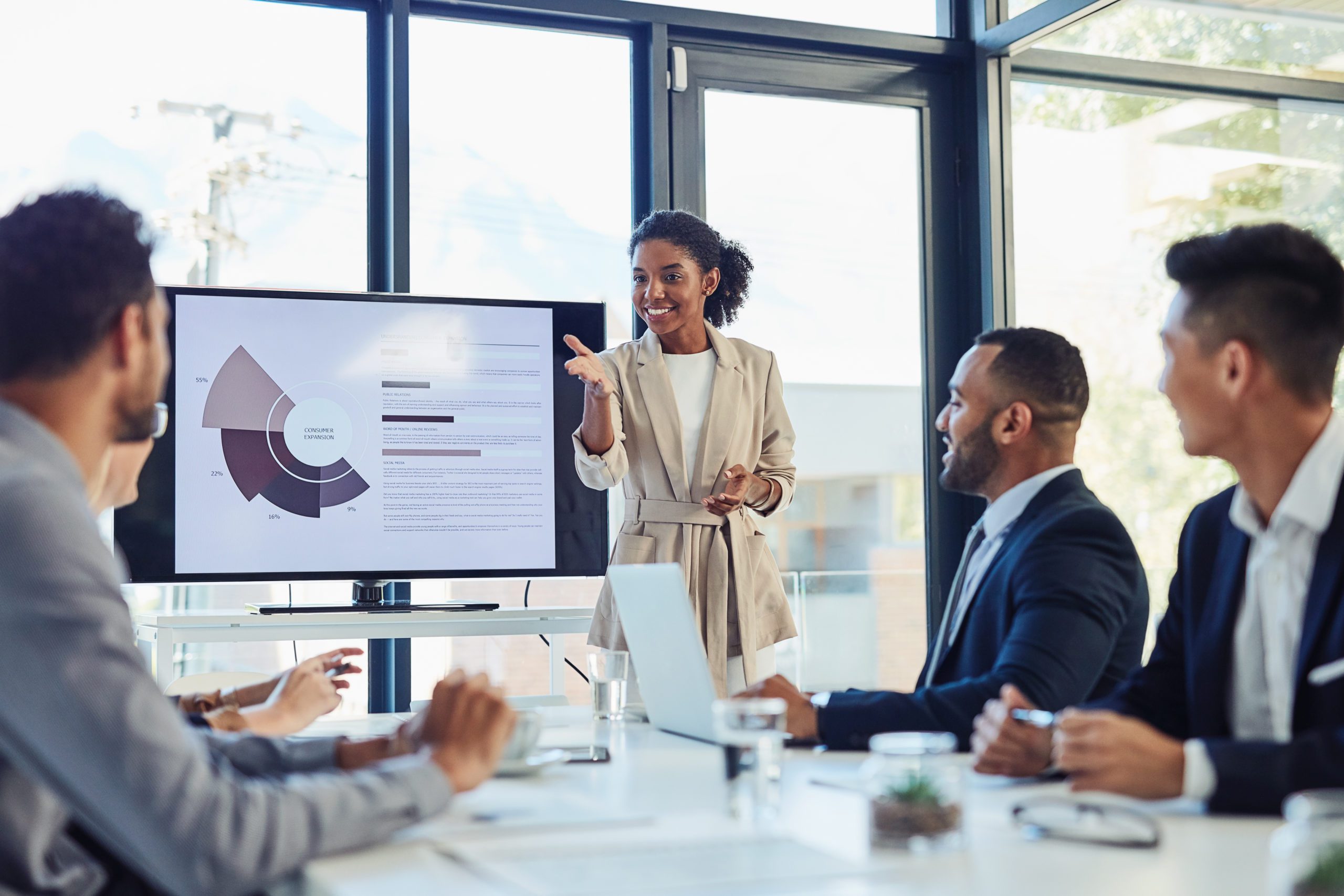Business meeting, businesswoman and presentation on screen of tv in modern boardroom with colleagues. Workshop, speech and black woman or speaker speaking with coworkers in conference room.